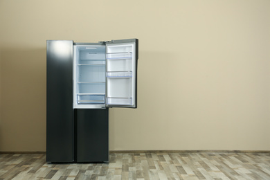 Modern refrigerator near beige wall, space for text