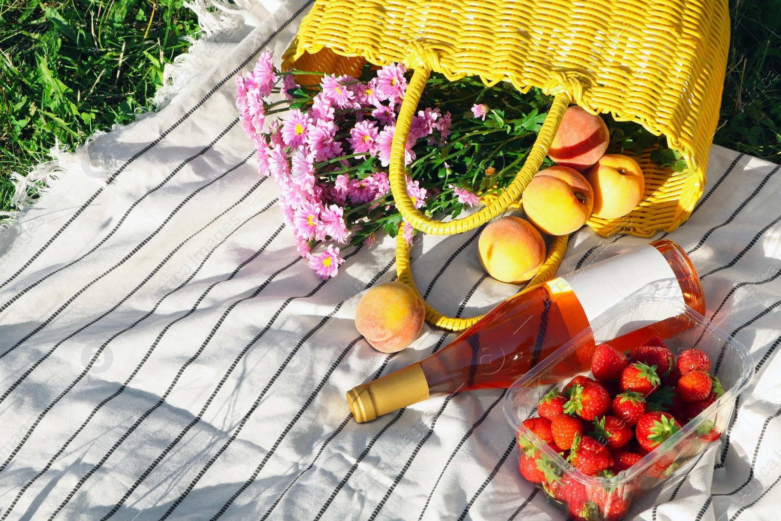 Photo of Yellow wicker bag with beautiful flowers, bottle of wine and food on picnic blanket outdoors
