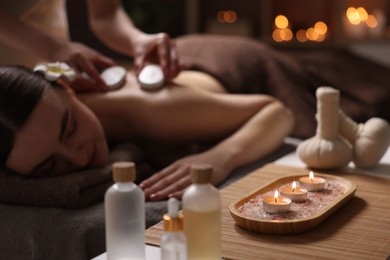 Spa therapy. Beautiful young woman lying on table during hot stone massage in salon, focus on burning candles