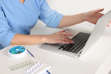 Doctor with laptop and pills at desk indoors, closeup. Online medicine concept