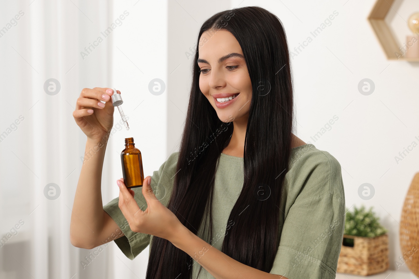 Photo of Beautiful woman holding bottle of serum in room. Cosmetic product