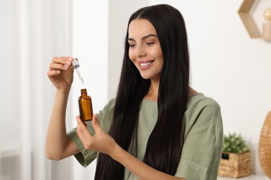 Beautiful woman holding bottle of serum in room. Cosmetic product