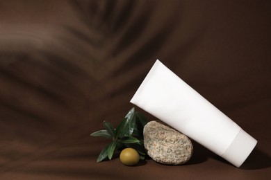 Photo of Tube of natural cream, stone and olive on brown background. Cosmetic products