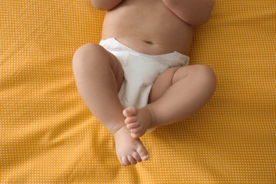 Photo of Cute little baby in diaper on yellow blanket, top view