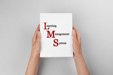 Woman holding book with text Learning Management System and red initial letters forming initialism LMS on white background, closeup