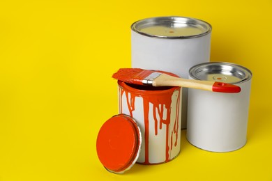 Photo of Cans of orange paint and brush on yellow background. Space for text