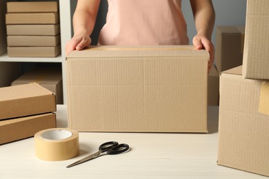 Packaging goods. Woman with cardboard boxes at white table indoors, closeup