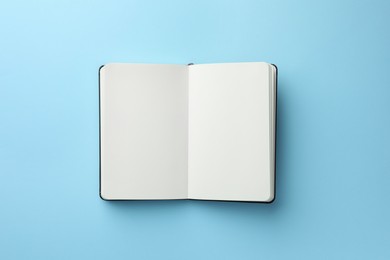 Open notebook with blank pages on light blue background, top view. Space for text