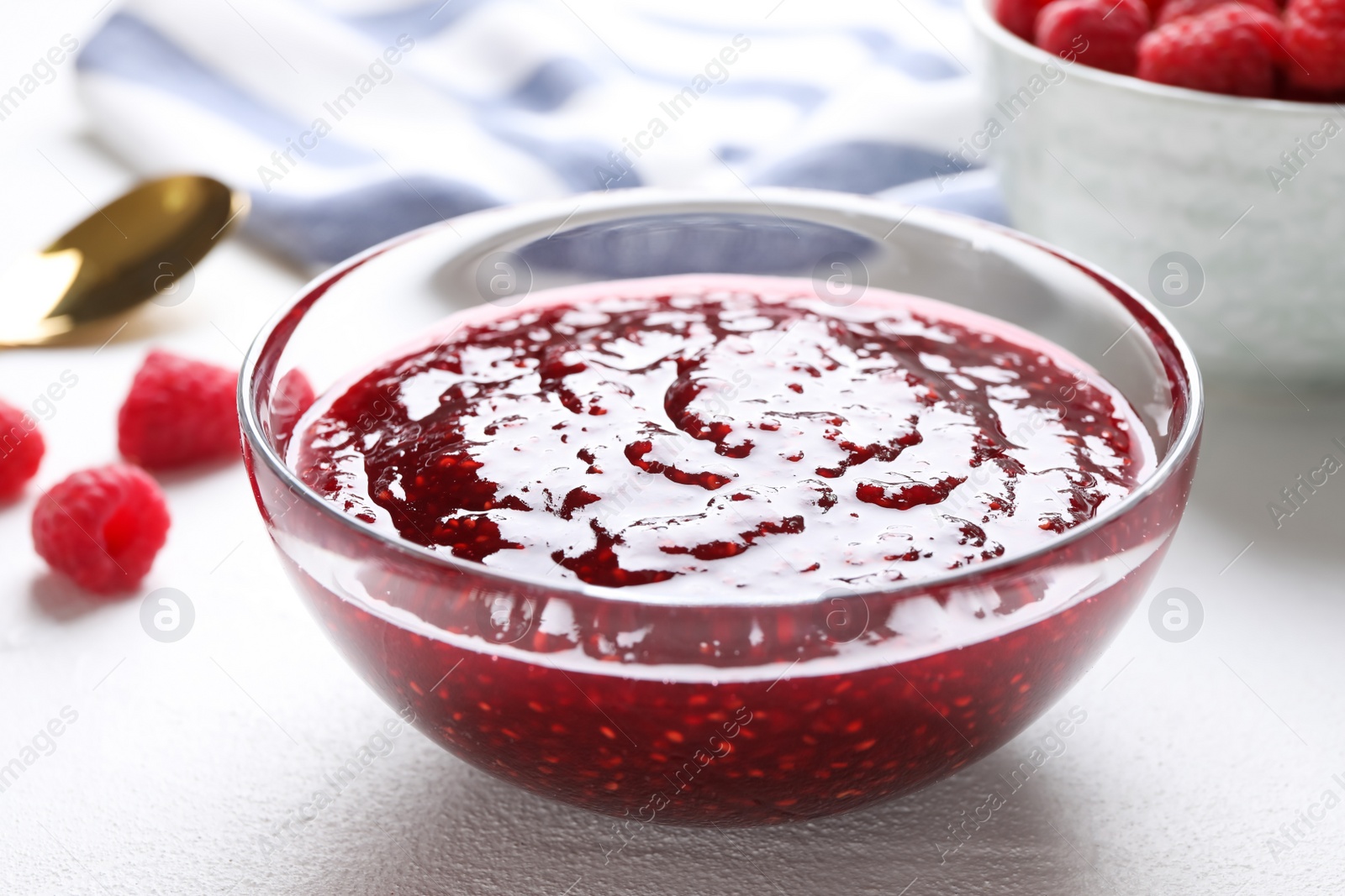 Photo of Delicious raspberry jam in glass bowl on white table