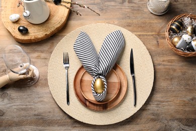 Photo of Festive table setting with painted eggs, plates and cutlery, flat lay. Easter celebration