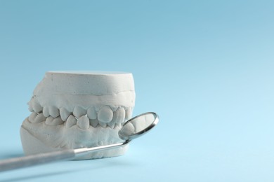 Photo of Dental model with gums and dentist mirror on light blue background, space for text. Cast of teeth