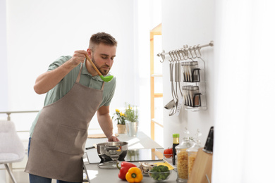 Photo of Young man cooking delicious soup in kitchen