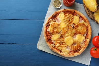 Photo of Delicious pineapple pizza and ingredients on blue wooden table, flat lay. Space for text