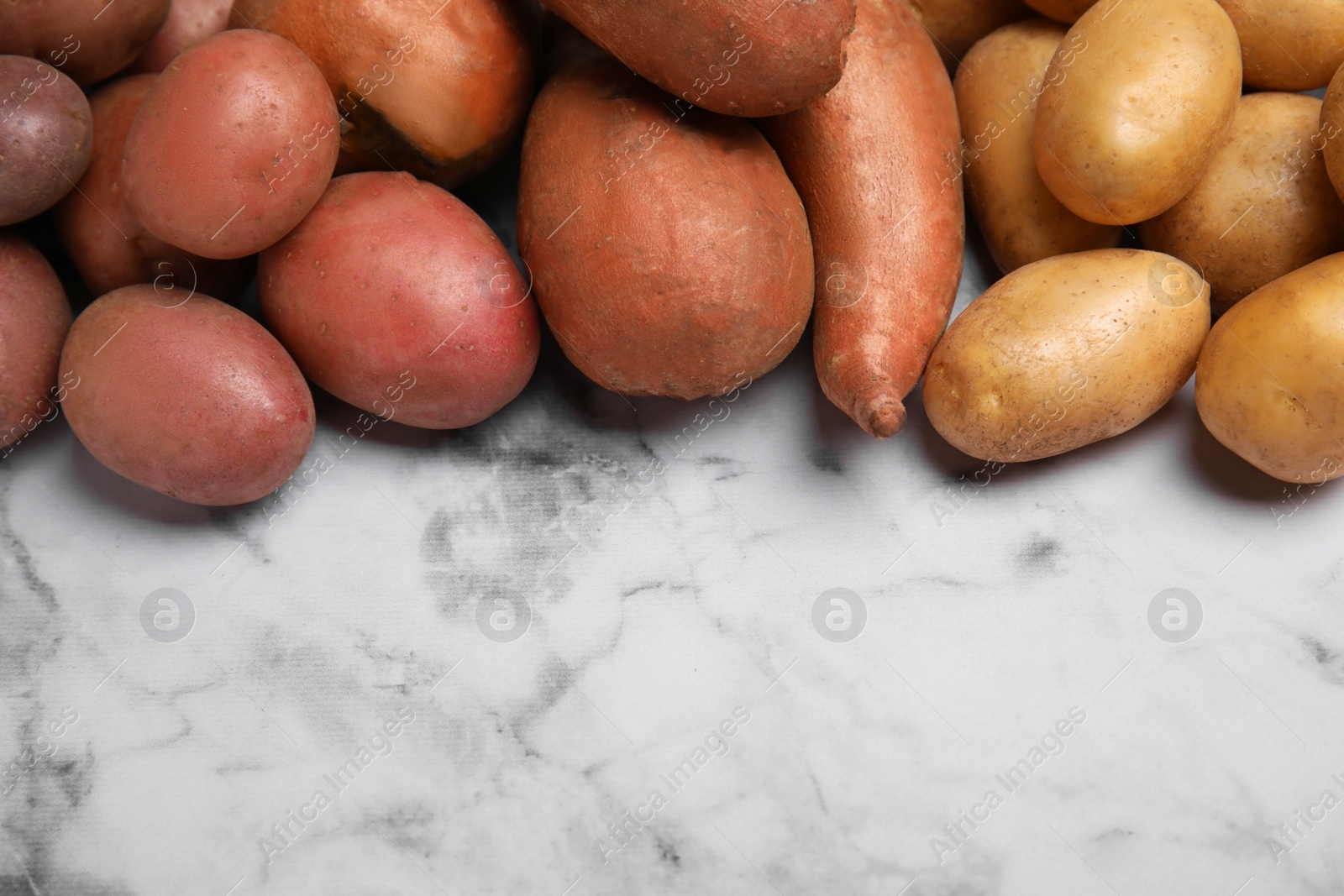 Photo of Different types of fresh potatoes on white marble table, space for text