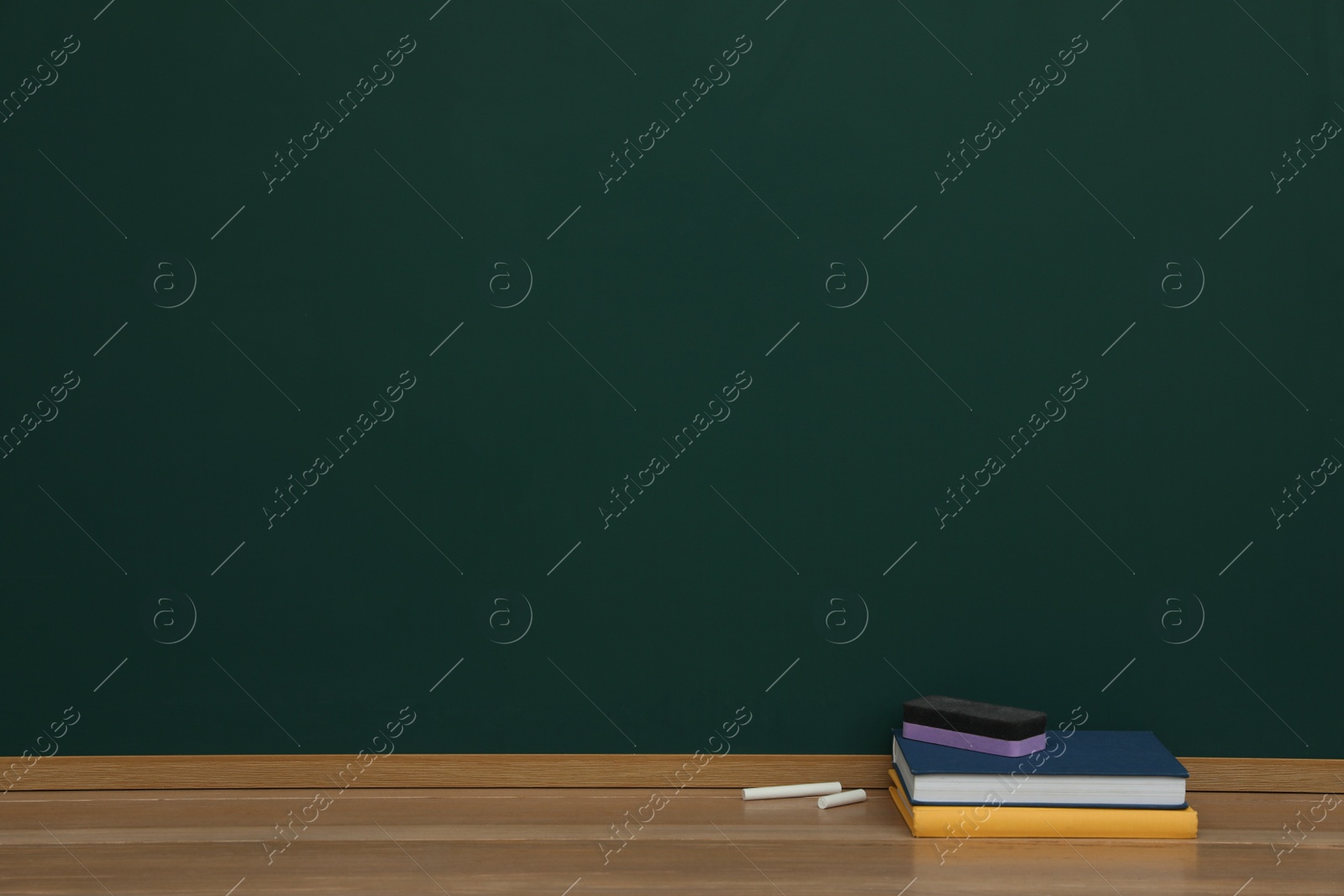 Photo of Books, pieces of chalk and duster on wooden table near greenboard, space for text