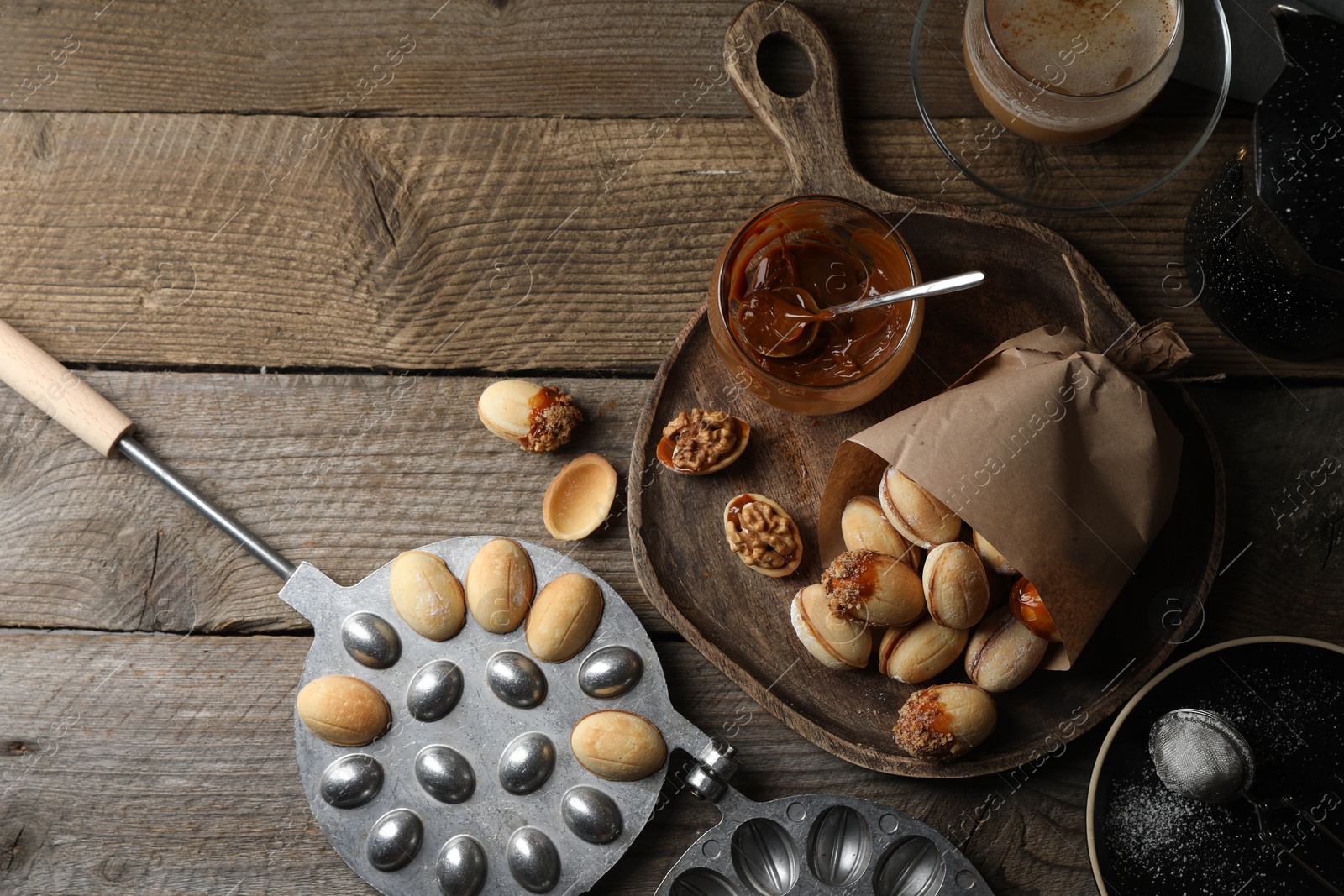 Photo of Freshly baked homemade walnut shaped cookies, boiled condensed milk, baking dish and cup of coffee on wooden table, flat lay. Space for text