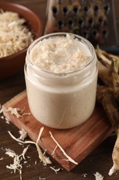 Photo of Spicy horseradish sauce in jar on wooden table, closeup