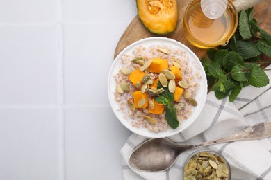 Photo of Tasty wheat porridge with pumpkin and mint in bowl served on white table, flat lay. Space for text