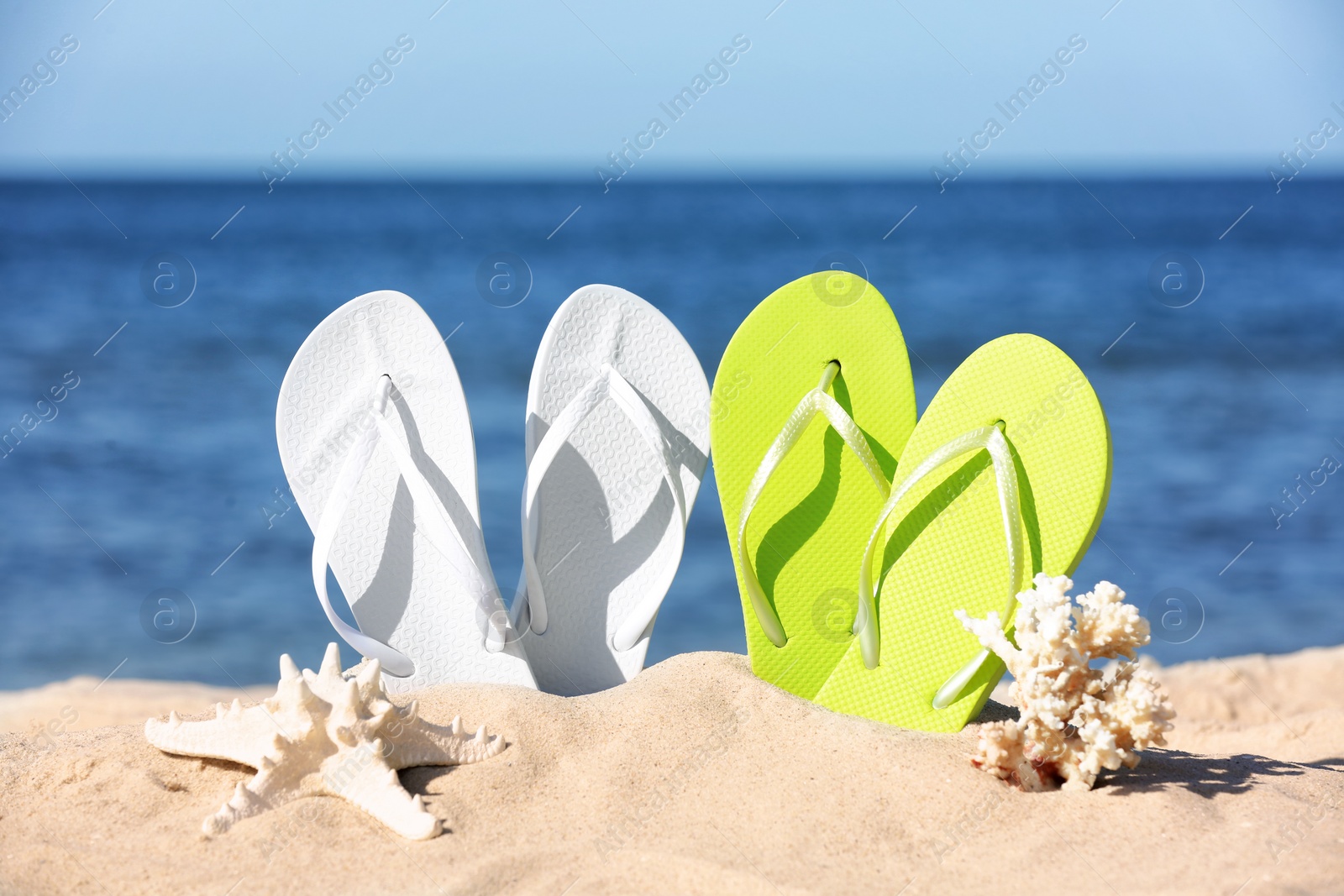 Photo of Composition with bright flip flops on sand near sea in summer. Beach accessories