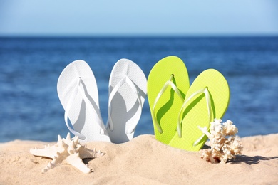 Photo of Composition with bright flip flops on sand near sea in summer. Beach accessories