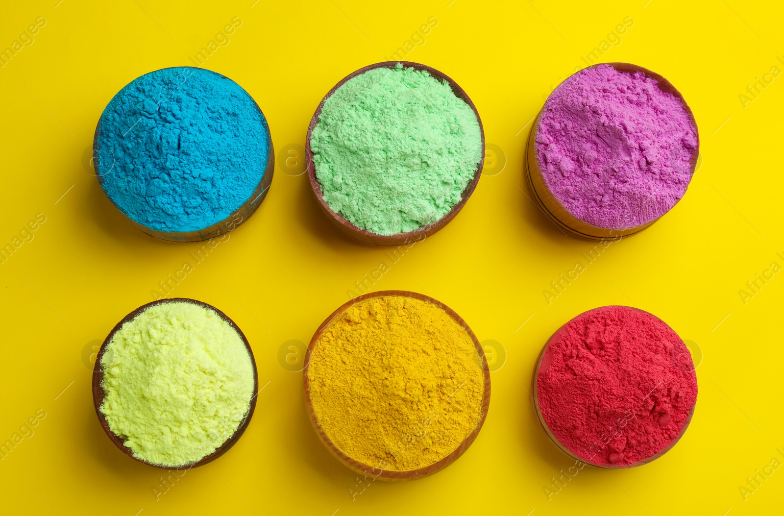 Photo of Colorful powders in bowls on yellow background, flat lay. Holi festival celebration