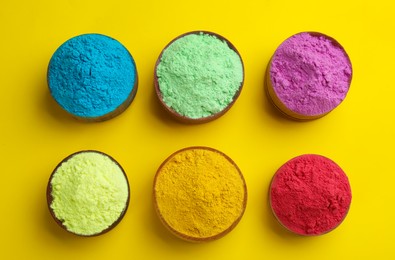 Photo of Colorful powders in bowls on yellow background, flat lay. Holi festival celebration