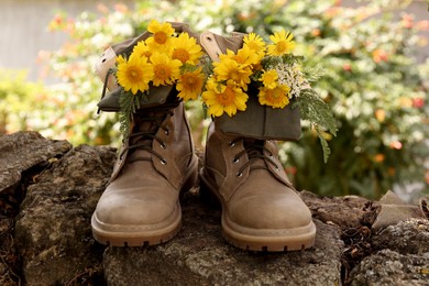 Boots with beautiful yellow flowers on stone outdoors