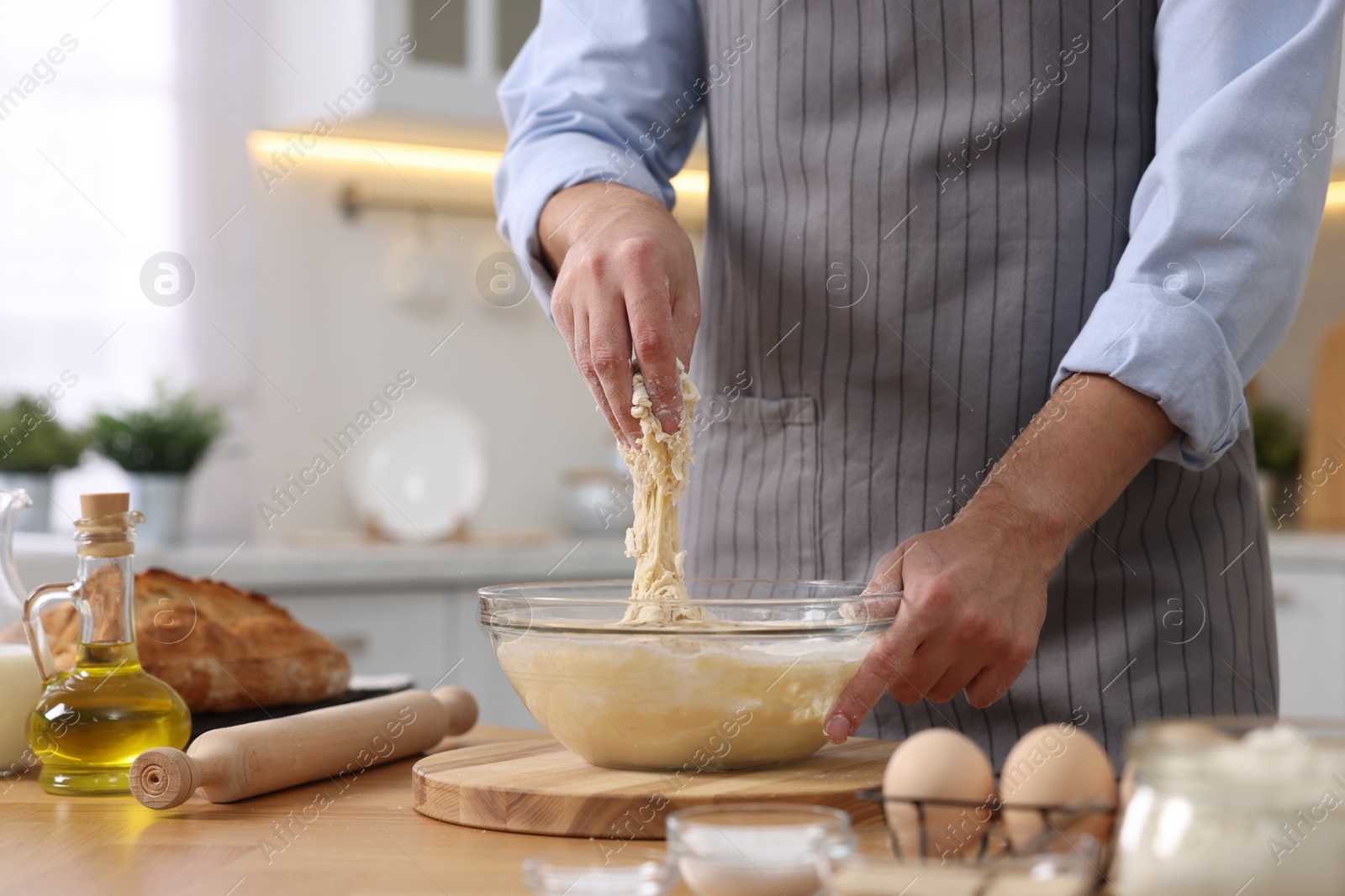 Photo of Making bread. Man preparing dough at wooden table in kitchen, closeup