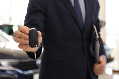 Salesman with key and clipboard in car salon, closeup