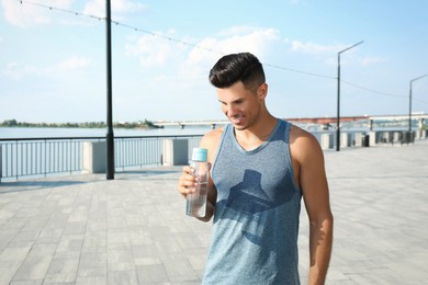 Handsome man in sportswear with bottle of water outdoors on sunny day