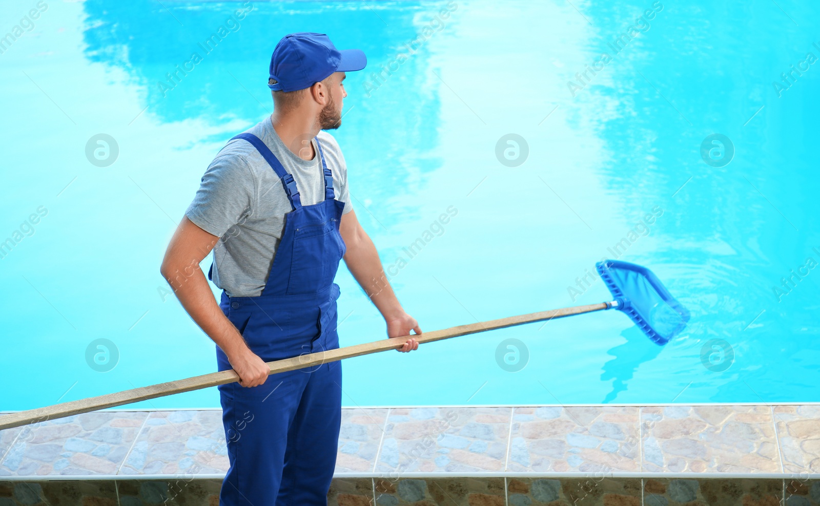 Photo of Male worker cleaning outdoor pool with scoop net