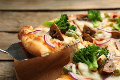 Photo of Taking piece of delicious vegetarian pizza at wooden table, closeup