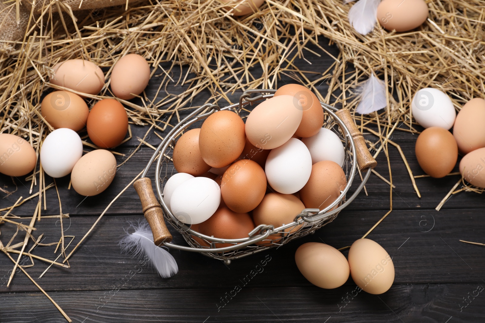 Photo of Fresh chicken eggs and dried straw on black wooden table, flat lay