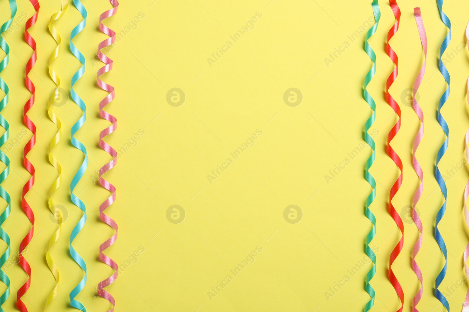 Photo of Colorful serpentine streamers on yellow background, flat lay. Space for text