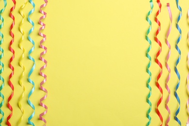 Photo of Colorful serpentine streamers on yellow background, flat lay. Space for text