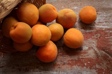 Photo of Delicious ripe apricots with wicker basket on wooden table, closeup