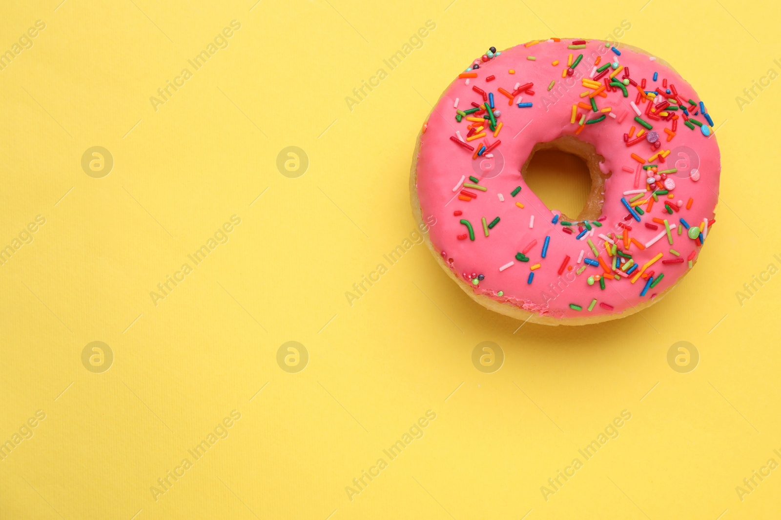 Photo of Glazed donut decorated with sprinkles on yellow background, top view. Space for text. Tasty confectionery