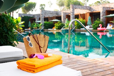 Photo of Wicker bag with beach accessories on sunbed near outdoor swimming pool, space for text. Luxury resort