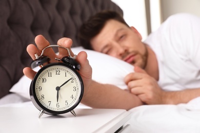Photo of Sleepy man turning off alarm clock on nightstand. Bedtime