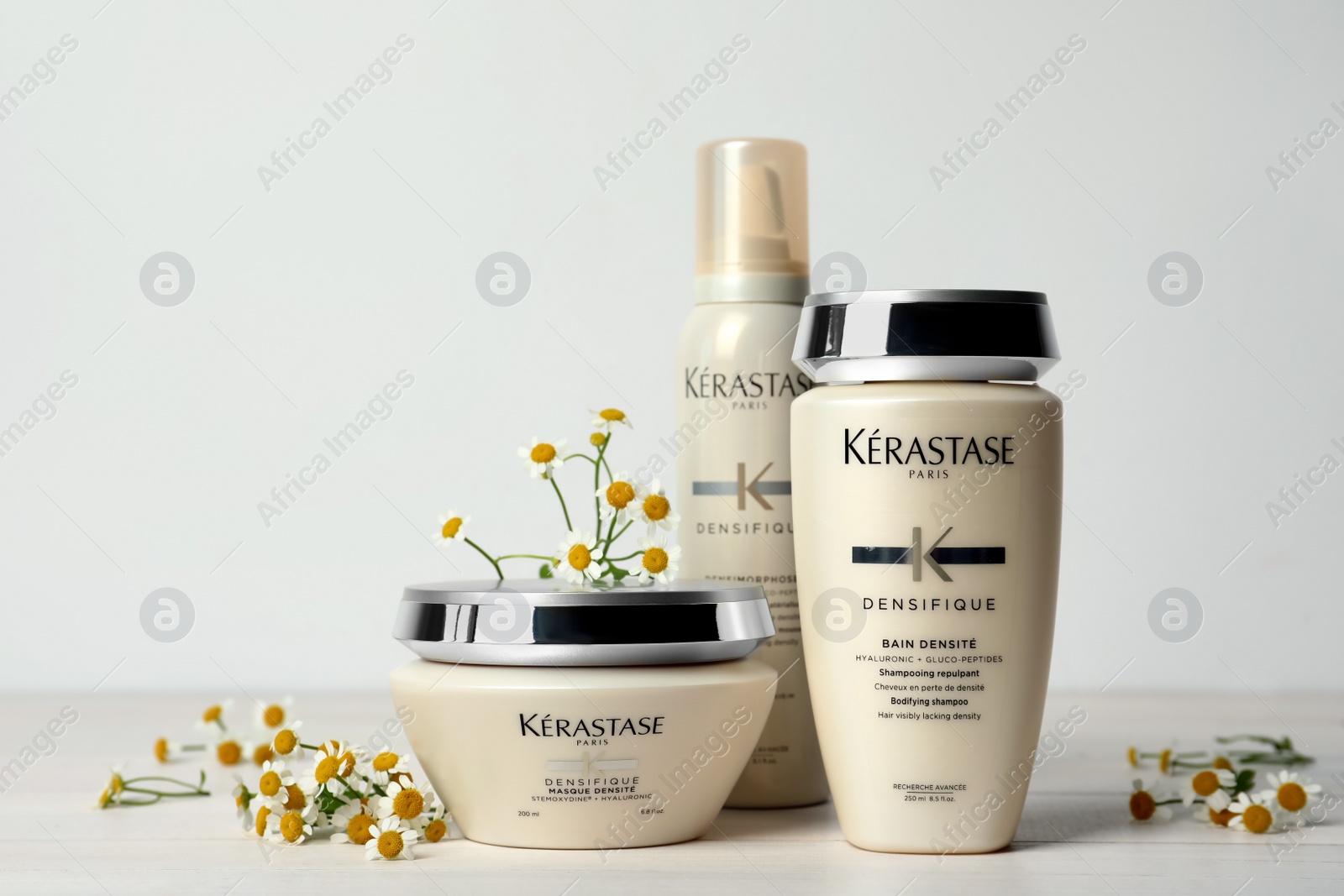 Photo of MYKOLAIV, UKRAINE - SEPTEMBER 07, 2021: Set of Kerastase hair care cosmetic products and chamomile flowers on white wooden table