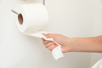 Woman taking toilet paper from roll holder on white wall, closeup