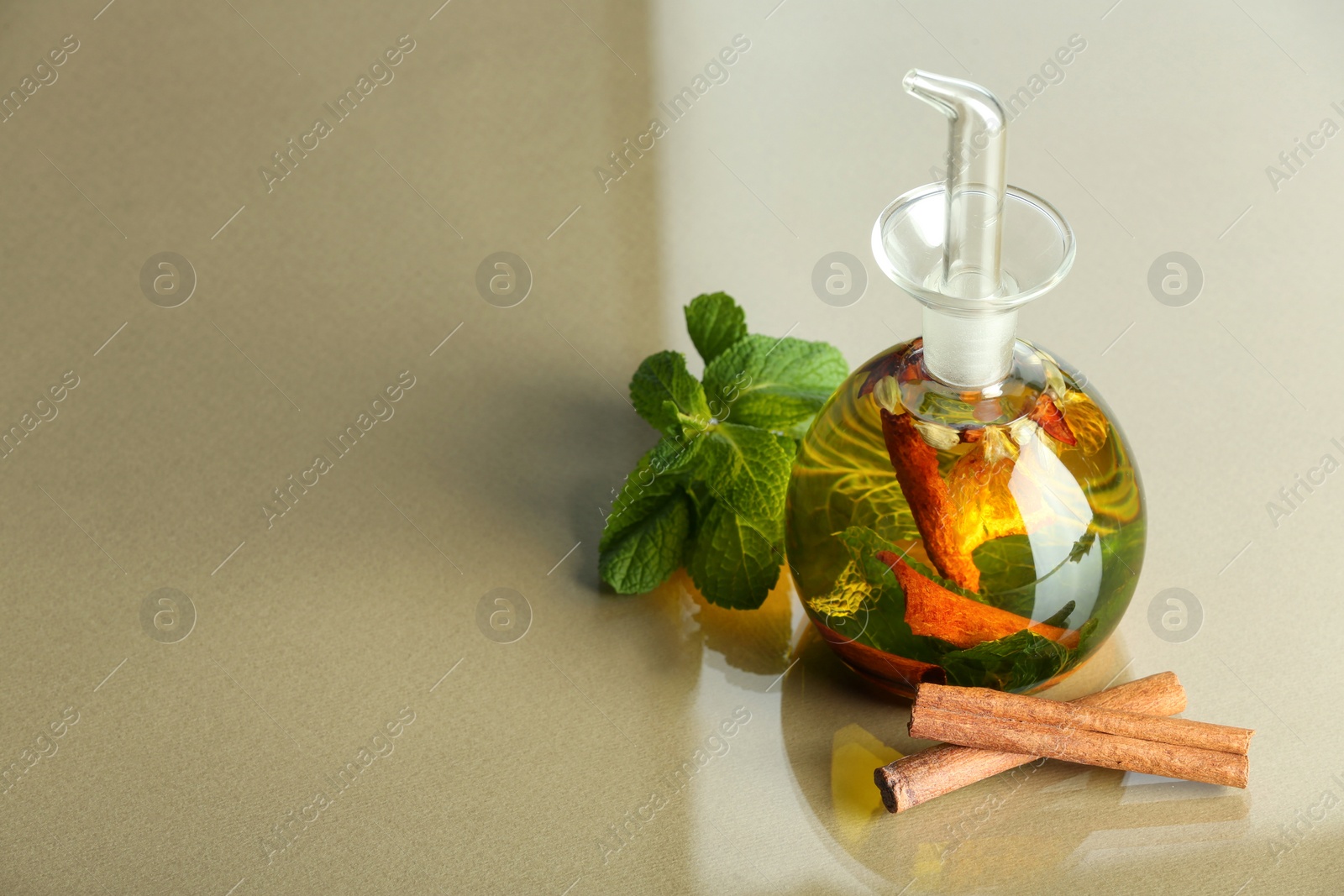 Photo of Cooking oil with spices and herbs in bottle, mint and cinnamon sticks on colorful table. Space for text