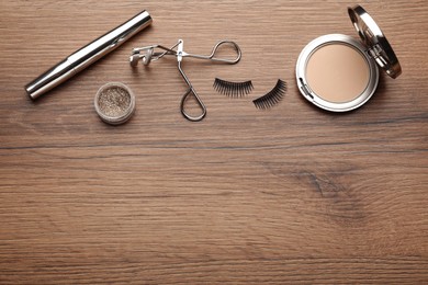 Photo of Flat lay composition with eyelash curler, makeup products and accessories on wooden table. Space for text