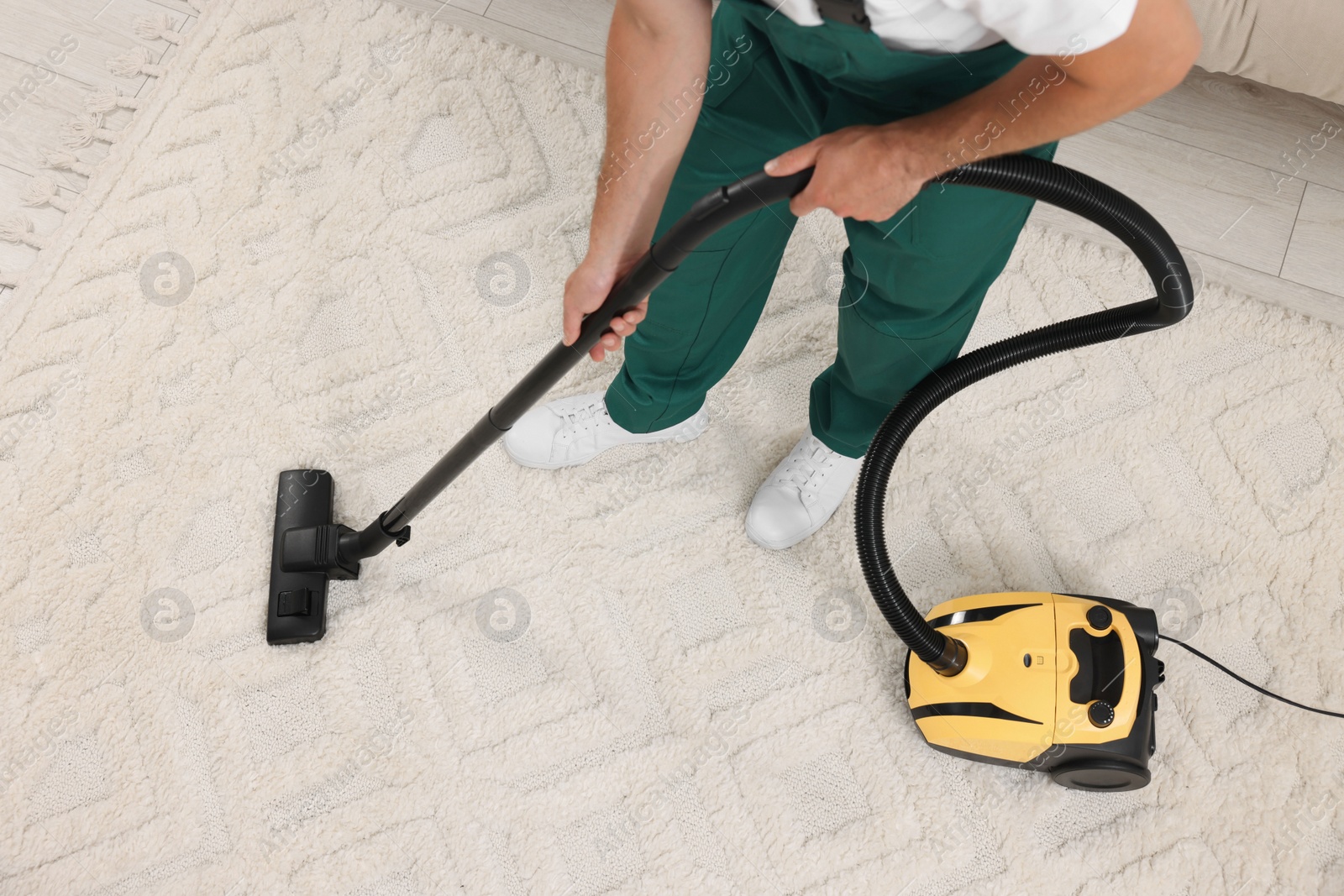 Photo of Dry cleaner's employee hoovering carpet with vacuum cleaner indoors, above view