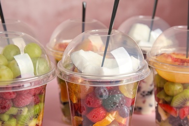 Photo of Fresh tasty fruit salad in plastic cups on pink background, closeup