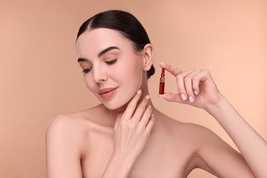 Photo of Beautiful young woman holding skincare ampoule on beige background