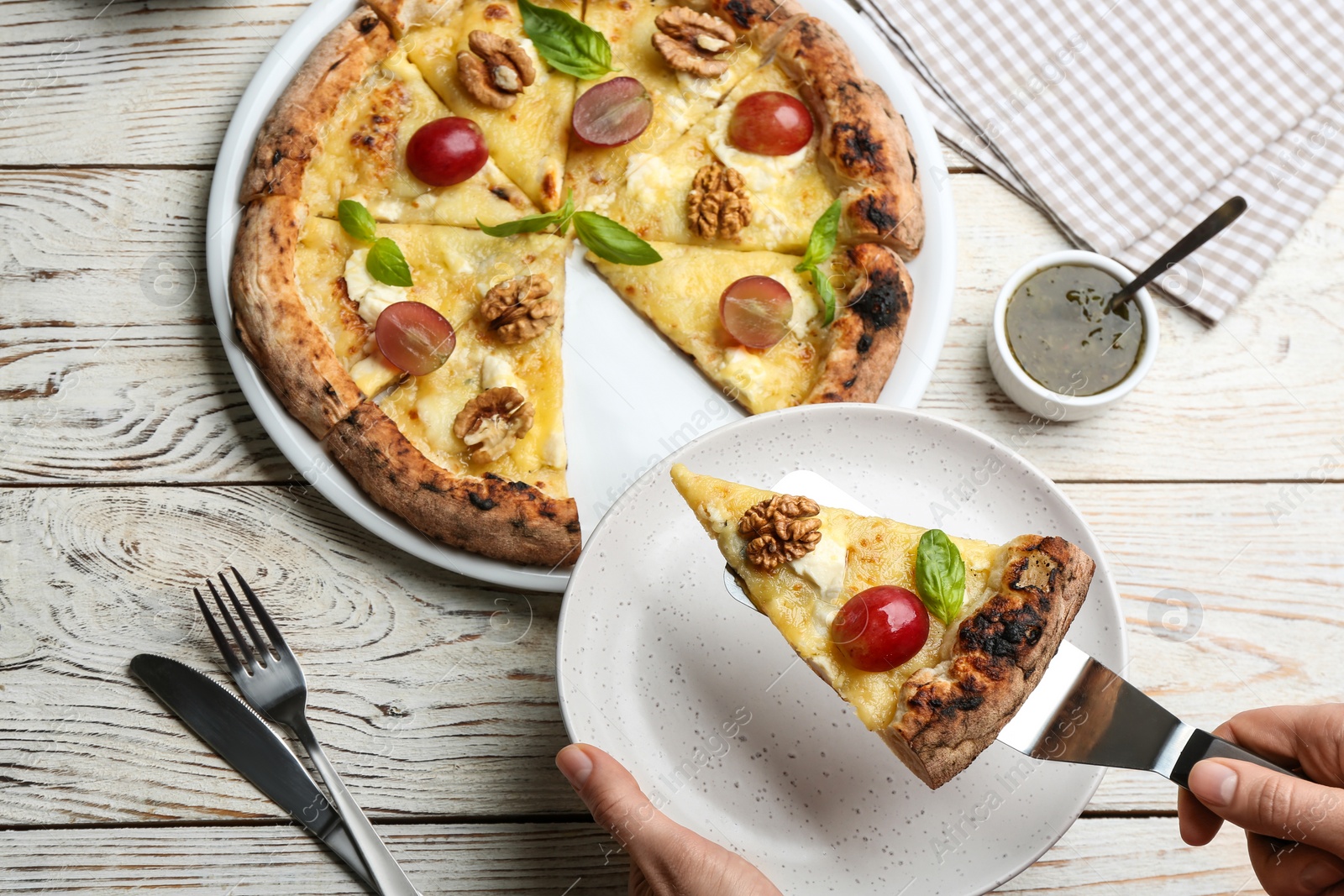 Photo of Woman taking slice of delicious cheese pizza with walnuts and grapes at white wooden table, top view