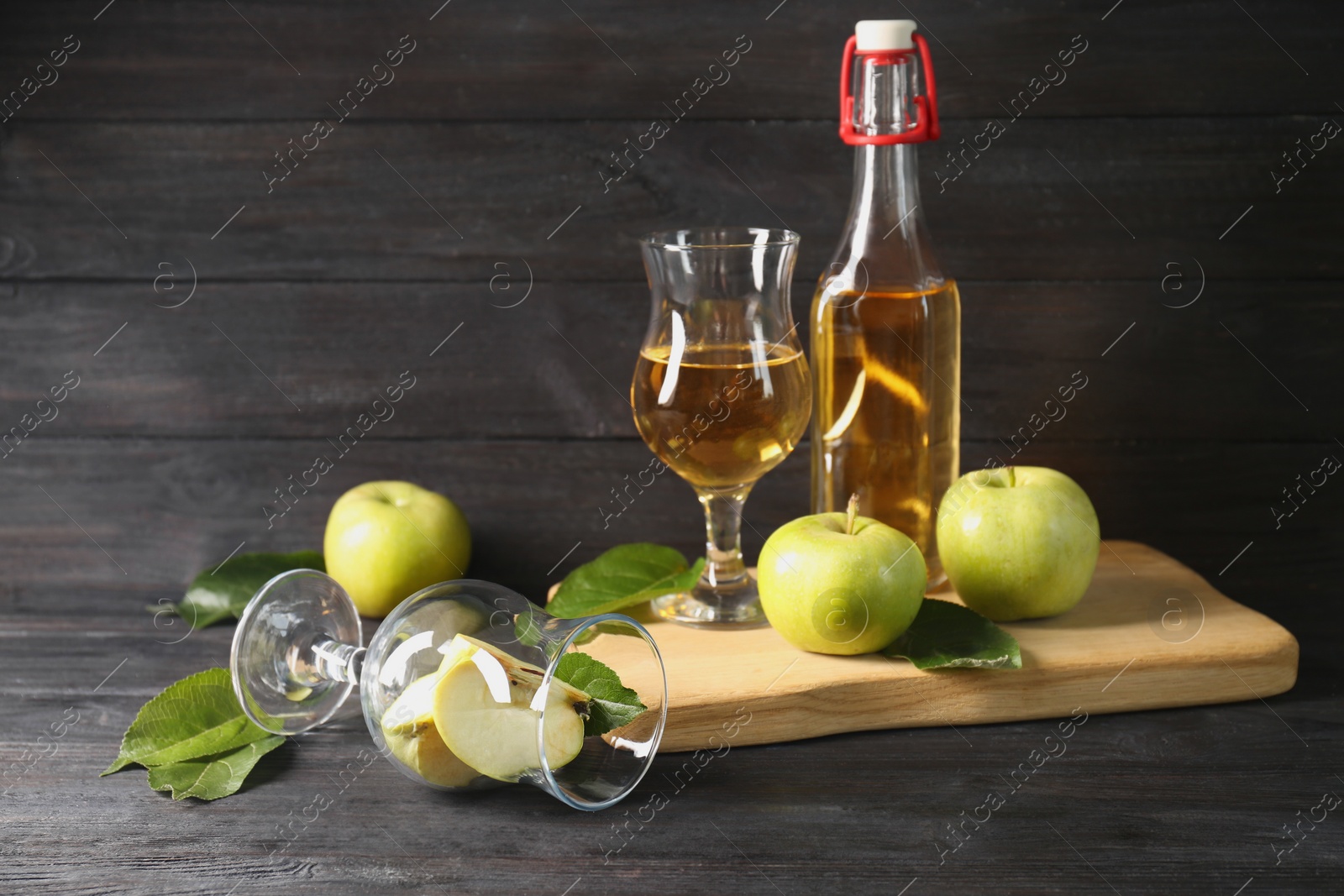 Photo of Delicious cider and apples with green leaves on black wooden table