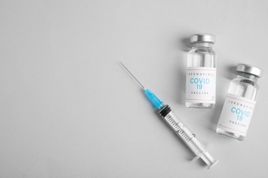 Photo of Vials with coronavirus vaccine and syringe on light background, flat lay. Space for text