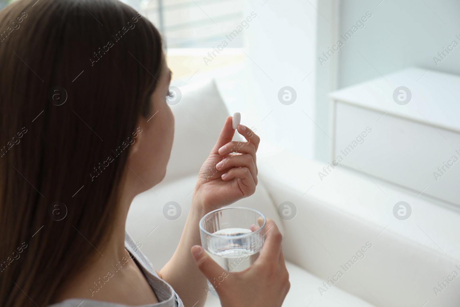 Photo of Young woman with glass of water taking pill at home, closeup